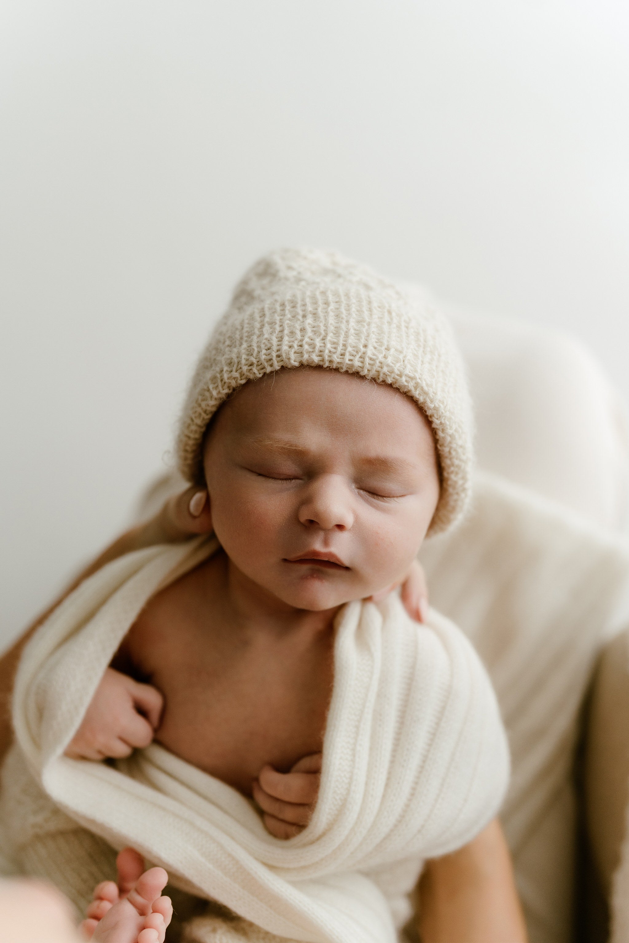 Newborn baby wrapped in a blanket and wearing a knitted hat against a white background